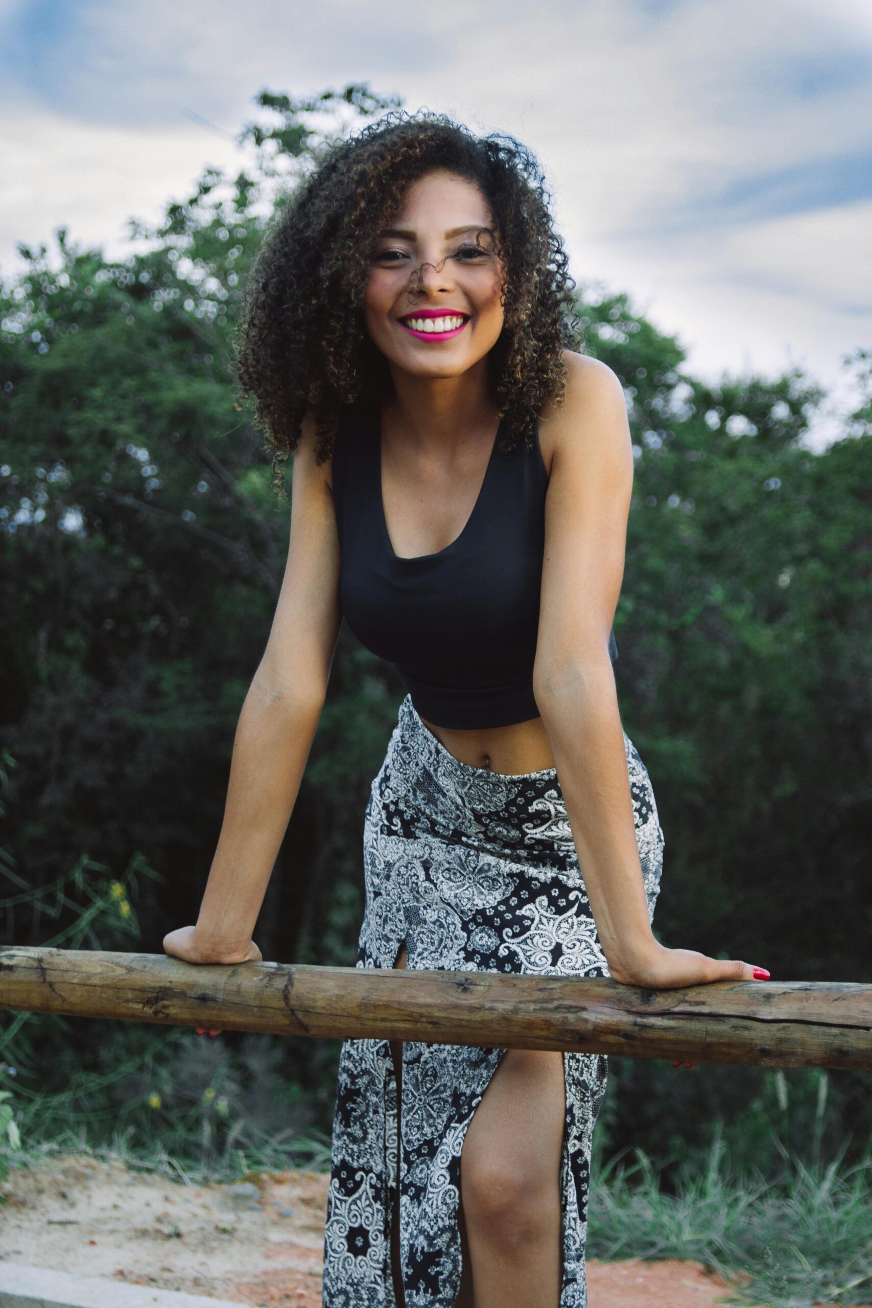 Young woman with curly hair smiling outdoors in casual fashion.